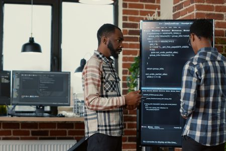 Team of software programmers leaving after analyzing source code on wall screen tv comparing errors using digital tablet. System engineers passing screens compiling code for artificial intelligence.